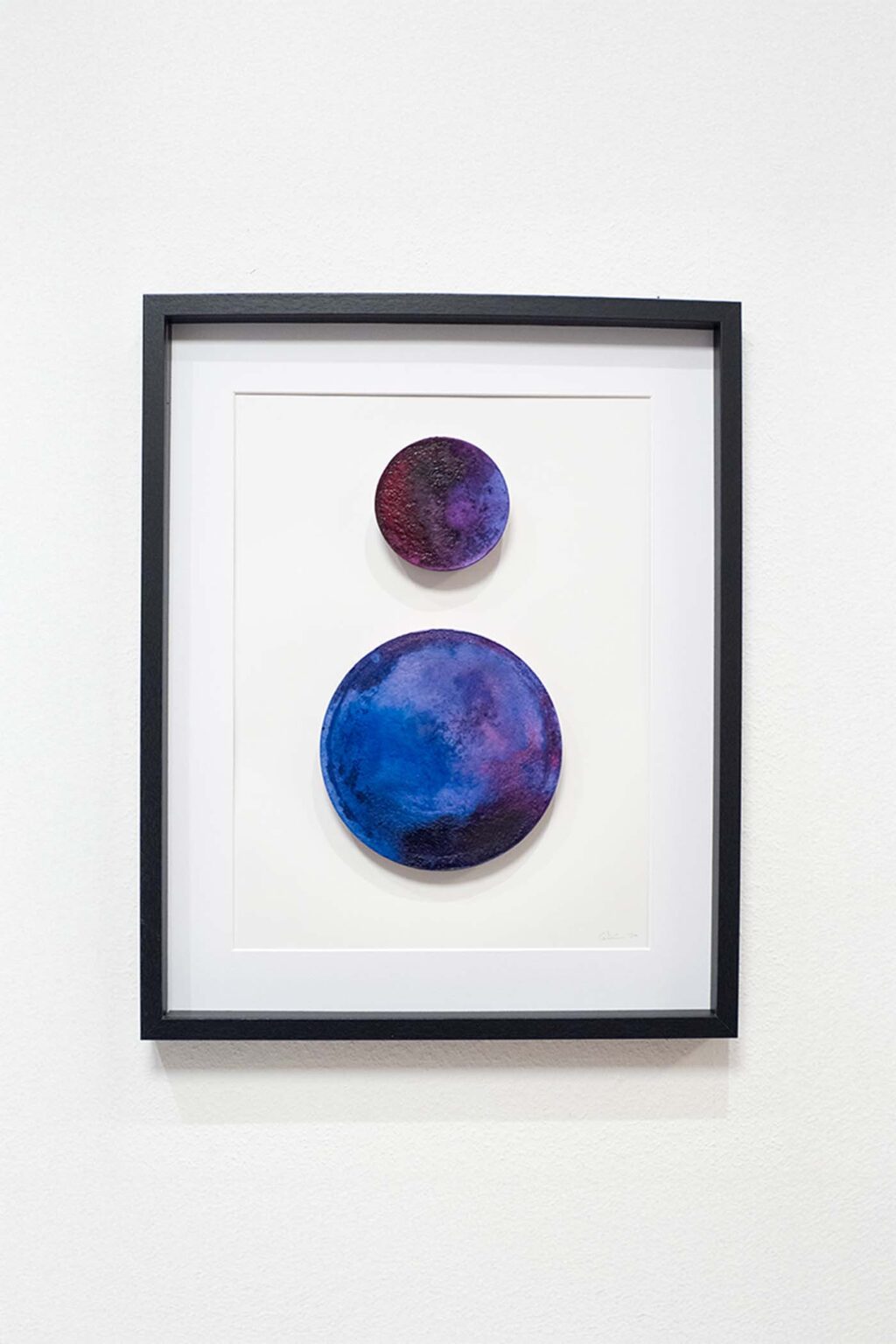 Gerahmtes Mixed-Media-Relief „Primal Bodies #2“ von Chris Cabrim: zwei kreisförmige Elemente in Blau/Violett auf weißem Passepartout.