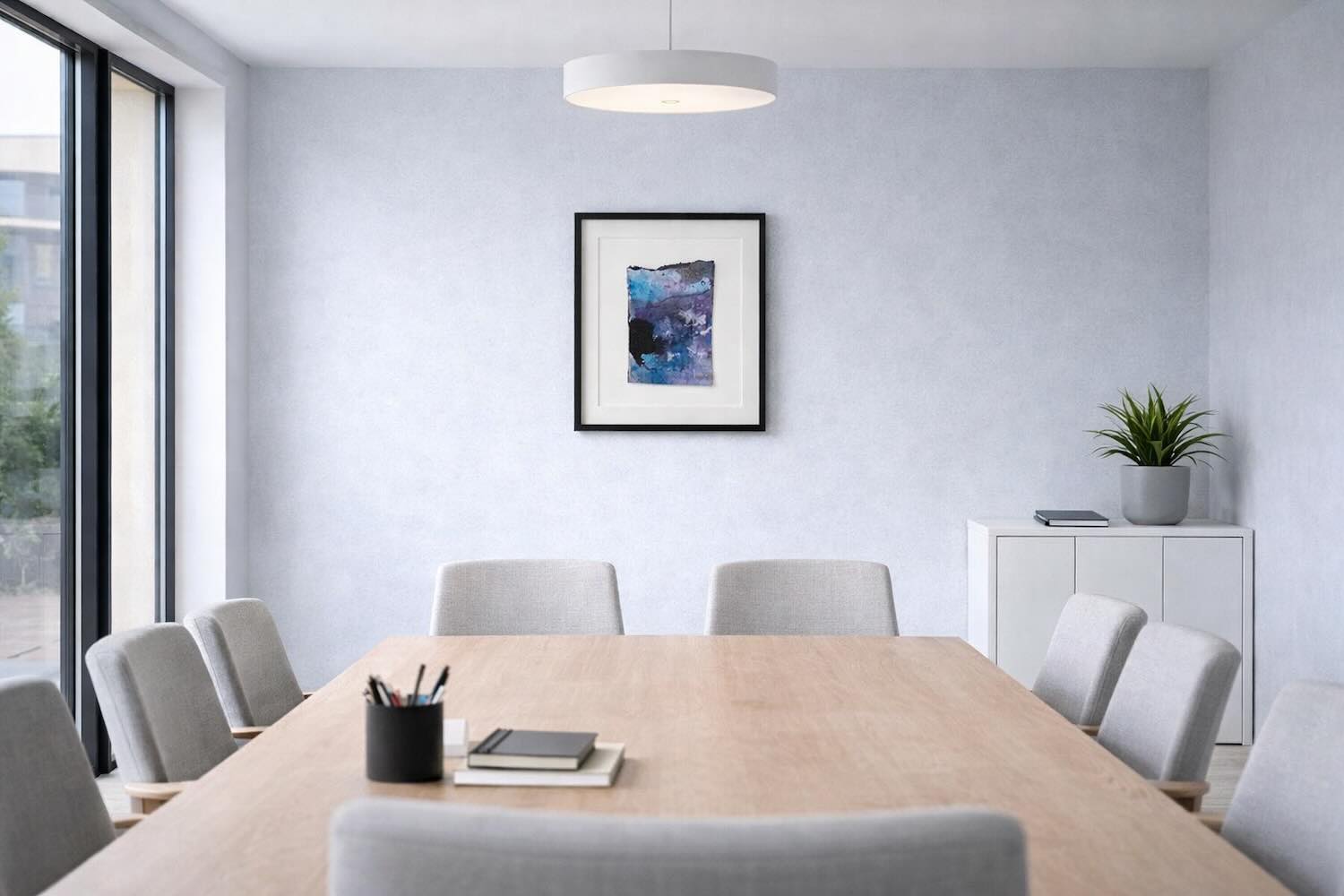 Heller Meetingraum mit großem Holztisch und grauen Stühlen; an der hellblauen Wand hängt ein gerahmtes abstraktes Kunstwerk in Blau-Violett-Tönen (Beispielvisualisierung).