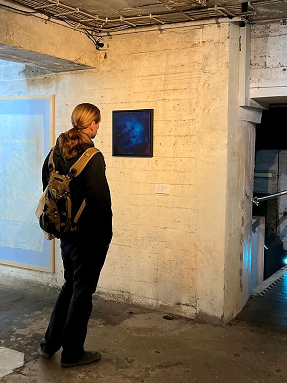 Besucher betrachtet ein gerahmtes Galaxies-Werk von Chris Cabrim an einer Betonwand im Bunker 101 während der Kunstroute Ehrenfeld 2026.
