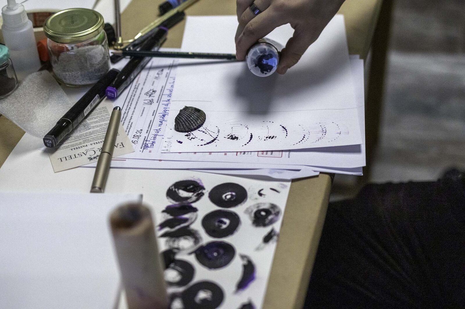Praktischer Materialversuch im Kunstworkshop Material Labor. Eine teilnehmende Person untersucht, welche wiederholbaren Spuren ein strukturiertes Objekt mit Pigment auf Papier erzeugen kann. Variation und Beobachtung führen schrittweise zur abstrakten Bildfindung.