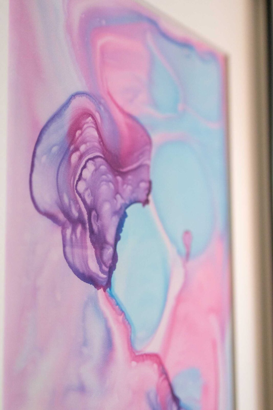 Nahaufnahme einer violetten Pigmentform. Ihre Ränder zeigen ringförmige Ablagerungen, wo Pigment beim Trocknen stehen geblieben ist. Umgeben von weichen Flächen in Türkis und Rosa.